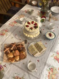 a table topped with cakes and pastries on top of a white table cloth covered in flowers