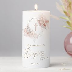 a white candle with a cross on it next to a pink vase filled with flowers