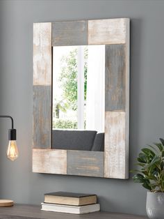 a wooden mirror hanging on the wall above a table with a book and lamp next to it