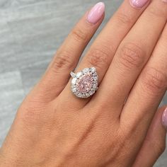 a woman's hand holding a pink diamond ring