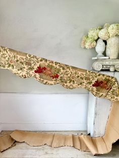 a piece of fabric sitting on top of a wooden floor next to a vase filled with flowers