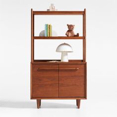 a teddy bear sitting on top of a wooden shelf next to a lamp and bookshelf