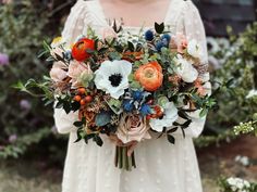 a woman holding a bouquet of flowers in her hands and wearing a white dress with an orange flower on it