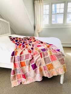 a bed with a blanket on top of it in a room next to a window