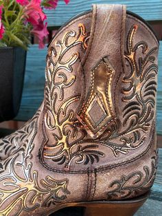 Delight in the beauty of these Corral Bone boots! A dazzling golden mirror-like overlay, stunning black embroidery, and classic zipper add style and flair. With a 7 1/4" shaft and 2" heel, plus a snip toe, these boots will turn heads with every step! Bone Golden mirror overlay Black embroidery Zipper 7 1/4" Shaft 2" Heel Snip Toe Western Gold Heeled Boots, Western Style Gold Heeled Boots, Mirror Overlay, Ankle Cowgirl Boots, Bone Boots, Golden Mirror, Studded Ankle Boots, Western Store, Black Embroidery