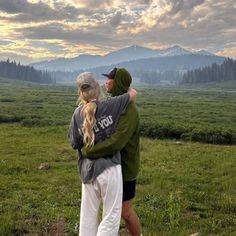 a man and woman standing on top of a lush green field with mountains in the background