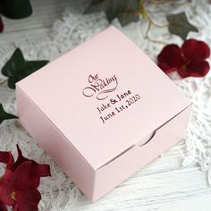 a pink wedding card box sitting on top of a lace tablecloth next to red flowers