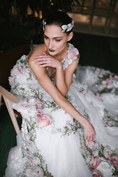 a woman in a white dress with flowers on it sitting down and looking at the camera