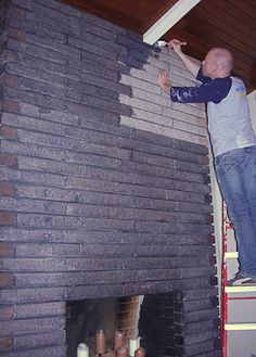 a man standing on top of a brick wall next to a fire place in a living room