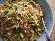 a blue bowl filled with rice and veggies next to a fork on top of a wooden table