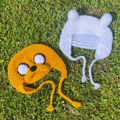 two crocheted hats with eyes and ears on the grass next to each other