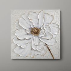 a white flower with gold in the center on a gray background, mounted to a wall