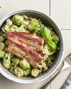 a bowl filled with meat and vegetables on top of a white table next to utensils