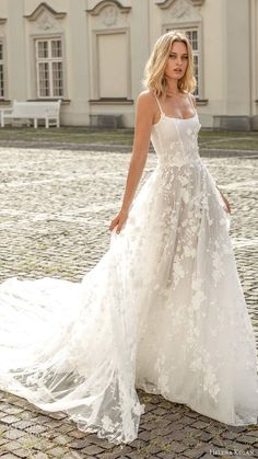 a woman in a white wedding dress standing on a cobblestone road with a building in the background