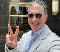 a man wearing sunglasses making the peace sign in front of a building with gold trim