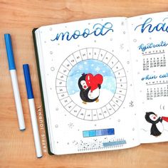 an open notebook with penguins and calendars on the pages, next to two pens