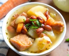 a white bowl filled with meat, potatoes and carrots next to an orange vegetable