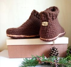 a pair of brown crocheted shoes sitting on top of a box next to pine cones