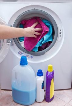 a person is washing clothes in a washer with detergents and bottles next to it