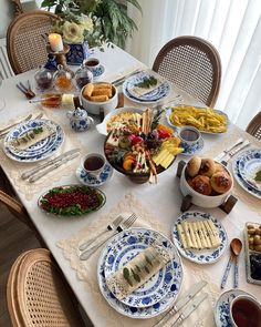 a table set with blue and white plates, silver utensils and food on it