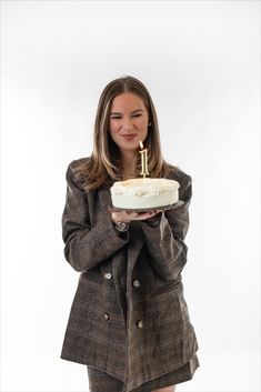 a woman holding a cake with a lit candle in her mouth while standing against a white background