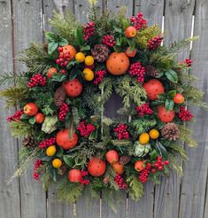 a christmas wreath with oranges, berries and pine cones hanging on a wooden fence