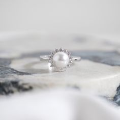 a pearl and diamond ring sitting on top of a table