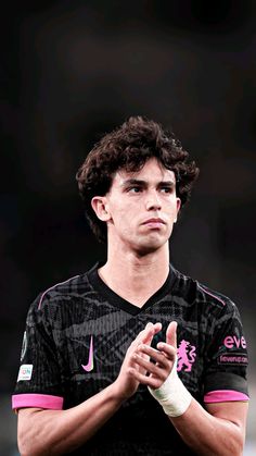 a young man wearing a black and pink soccer uniform with his hands clasped in front of him