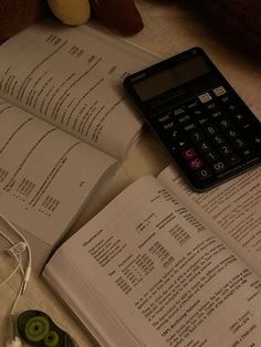 an open book, calculator and earbuds on a table with other books