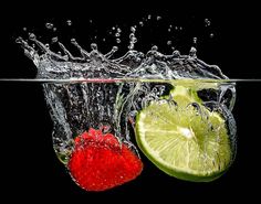 lime and strawberry splashing into water on black background, with one slice cut in half