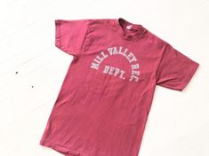 This t-shirt came from a friend who was a camp counselor in Mill Valley in the '70s.  It's a great vintage athletic tee and was barely worn, so it has lots of life left! Item details:- “Mill Valley Rec. Dept.” on front- burgundy cotton- round neckBest fits a size xxs - xs.Measurements:bust: 32”length: 25”shoulder: 15”sleeve: 6.5”Excellent vintage condition. Vintage College T-shirt With Lettering, Vintage Short Sleeve T-shirt With Lettering, Vintage T-shirt With Lettering For College, Vintage Lettering T-shirt For College, 70s Shirts, Camp Counselor, Mill Valley, Sport T-shirts, Graphic Tees Women