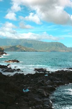 an ocean view with rocky shore and mountains in the background