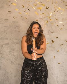 a woman in black pants holding a champagne bottle with confetti falling around her