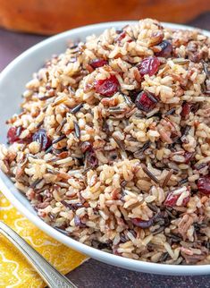 a bowl filled with rice and cranberries on top of a table next to an orange pumpkin