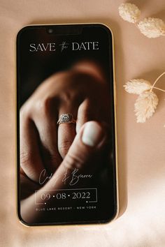 a phone with a wedding ring on it next to some dried flowers and a couple's engagement ring