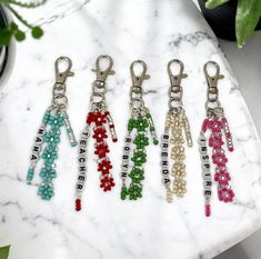 six keychains with beaded flowers on them sitting on a marble surface next to a potted plant