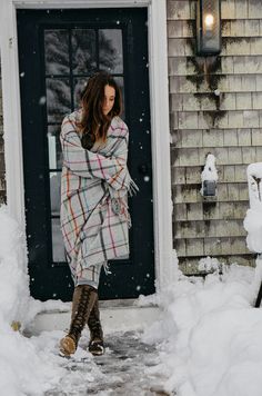 a woman standing in front of a door covered in snow with her arms wrapped up