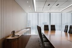 an empty conference room with wooden tables and black chairs in front of large window blinds