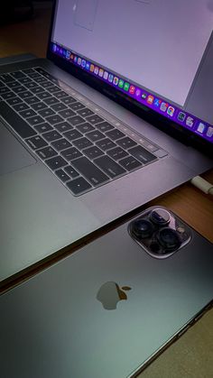 an open laptop computer sitting on top of a wooden desk next to a cell phone