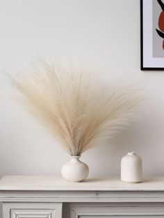 two white vases sitting on top of a table with some dry grass in them