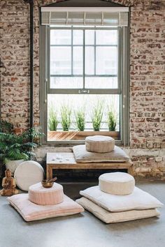 pillows and cushions are arranged on the floor in front of a brick wall with an open window