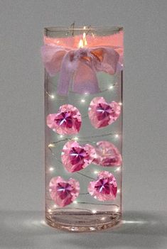 a glass vase filled with pink stones and a lit candle on top of the table