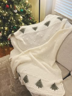 a christmas tree is in the corner of a living room next to a couch with a blanket on it