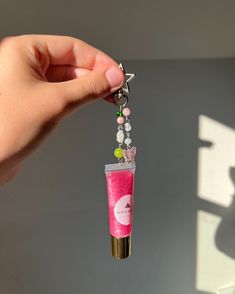 a hand holding a pink tube shaped keychain with beads and charms hanging from it