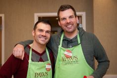 two men in green aprons standing next to each other with their arms around one another