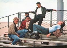 four men sitting on a bench in front of a chain link fence and one man standing