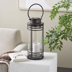 a black lantern sitting on top of a table next to a white chair and potted plant