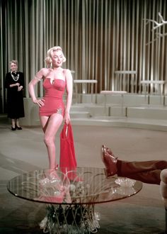 a woman in a red dress standing next to a glass table with a man sitting on it