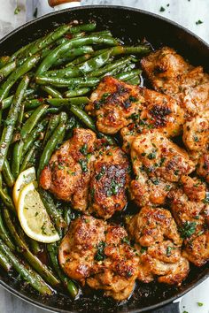 chicken and asparagus in a skillet with lemon wedges