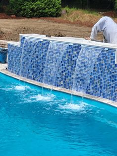 a man standing on top of a blue tiled wall next to a swimming pool filled with water